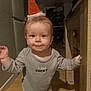 baby, child, indoor, wooden_table, floor, clothing, shirt, hat, santa_hat, face, expression, standing, hand, light, shadow, curious, person, young_child, home, flooring
