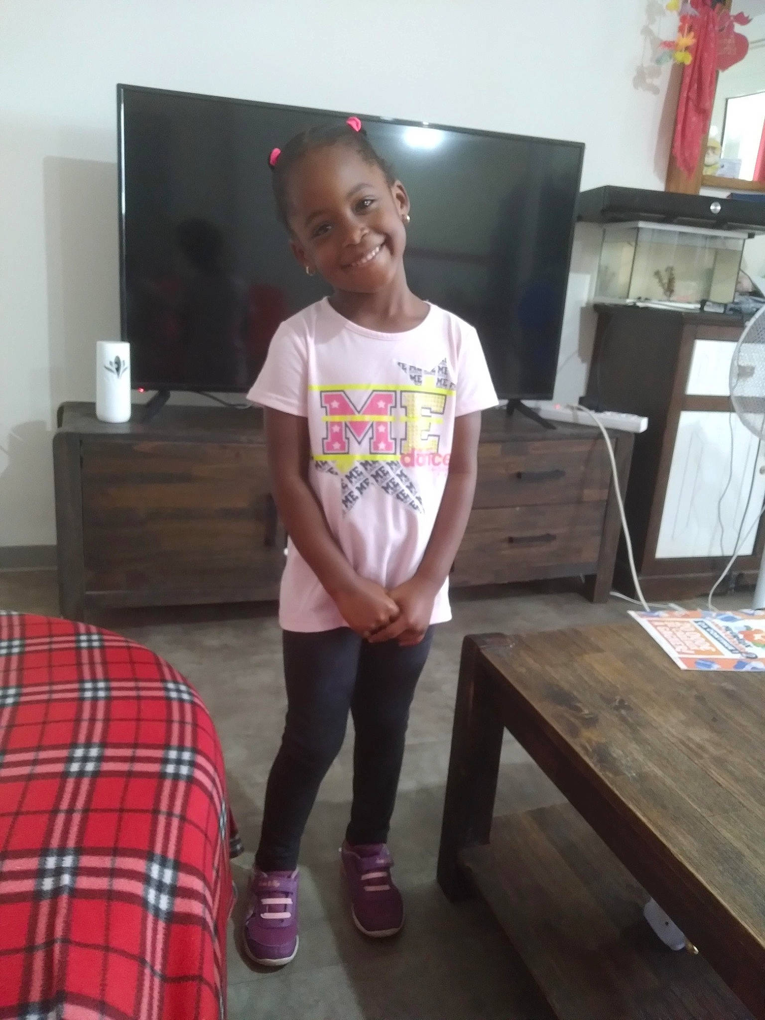 Lena a rejoint le concours — aidez-le/la à gagner de superbes lots ! chest_of_drawers, child, drawer, event, floor, flooring, furniture, hardwood, joy, living_room, person, plaid, shorts, smile, standing, t_shirt, table, tartan, television, textile