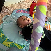 Lïon a rejoint le concours — aidez-le/la à gagner de superbes lots ! baby, infant, child, play_mat, toy, plush_toy, activity_gym, striped_pole, colorful, purple, gaze, lying_down, fuzzy_rug, carpet, denim_knee, onesie, expression_wide_eyes, hand, face, indoor