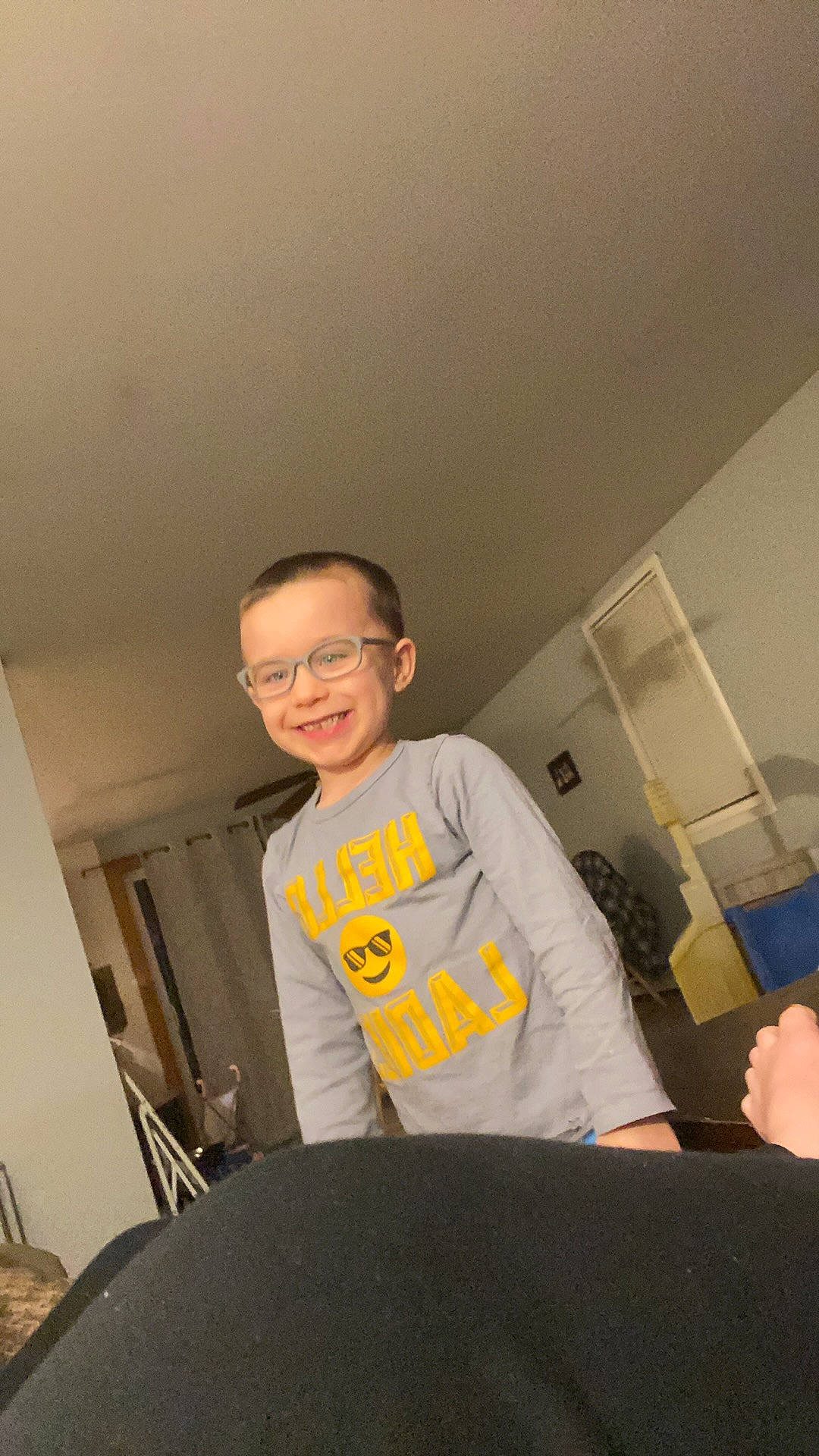 Jaxson is registered to the contest to win money with this photo: ceiling, chair, child, chin, elbow, eyewear, flooring, fun, glasses, happy, joy, person, room, shorts, sitting, sleeve, smile, t_shirt, toddler, top