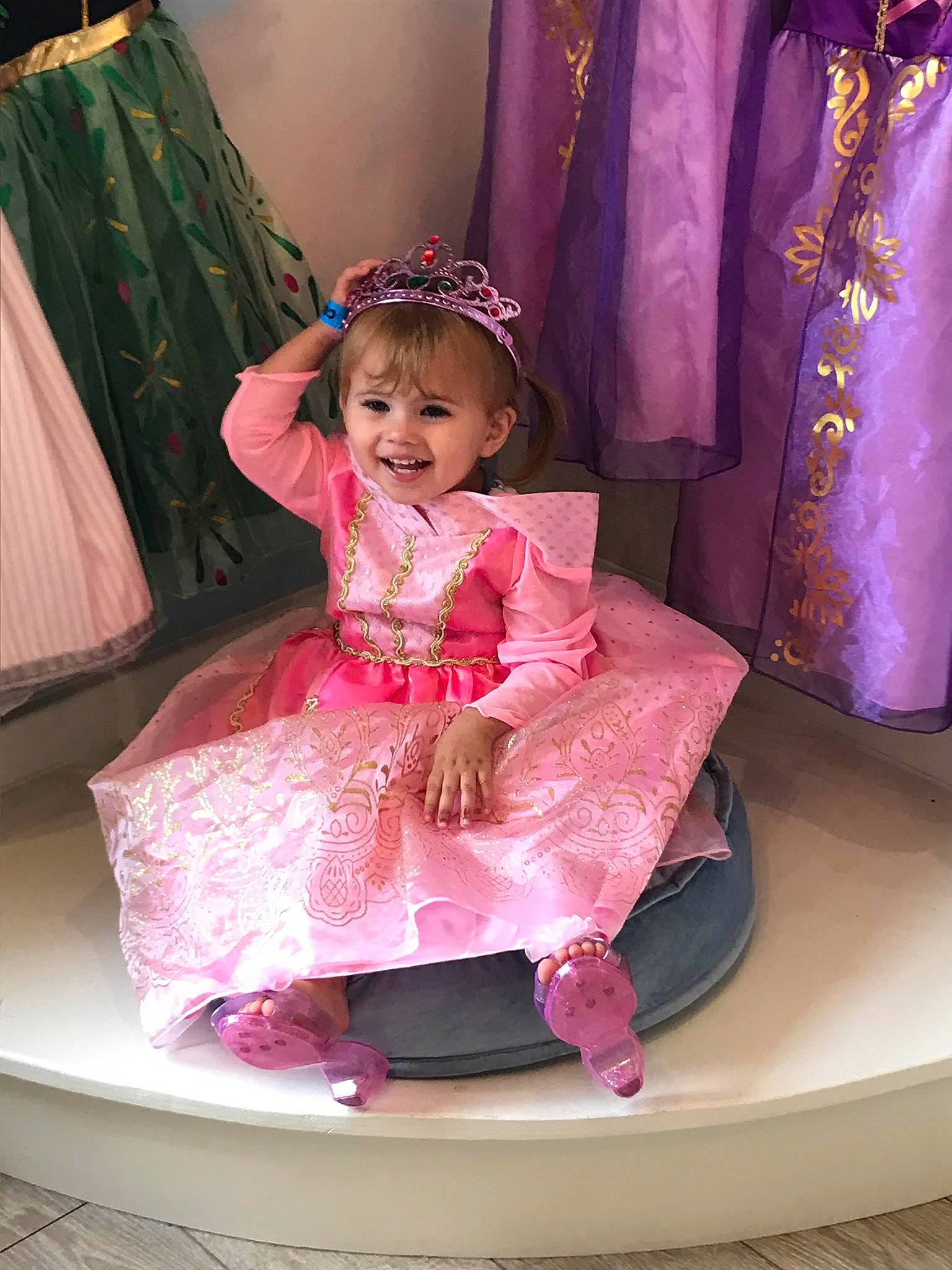 Phoenix is registered to the contest to win money with this photo: baby_toddler_clothing, chair, child, curtain, dress, embellishment, event, fashion_design, formal_wear, fun, happy, headpiece, joy, magenta, peach, person, pink, purple, room, smile