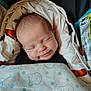 baby, newborn, smiling, sleeping, blanket, swaddled, car_seat, fabric, soft, infant, head, face, peaceful, cozy, child, wrapped, pattern, clothing, cute, resting