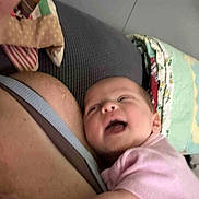 Estella is registered to the contest to win money with this photo: baby, infant, person, clothing, pink, arm, face, smile, joyful, adult, strap, quilt, fabric, background, closeup, candid, indoor, skin, hand, hug