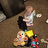 baby, child, carpet, toy, plush_toy, stuffed_animal, floor, indoor, person, sitting, clothing, play, cute, infant, young_child, carpeted_floor, toy_truck, black_cloth, room, home