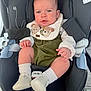 baby, infant, car_seat, child, footwear, bib, white_shoes, green_outfit, socks, face, hands, sitting, safety_harness, indoors, cute, expression, young_child, clothing, person, portrait