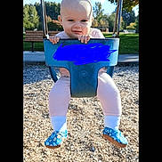 Hailey joined the competition — help win amazing prizes! baby, child, swing, playground, outdoor, daylight, park, blue_swing, pink_pants, shoes, wood_chips, trees, sky, expression, holding, seat, infant, clothing, fun, nature
