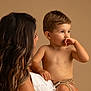 woman, child, toddler, holding, portrait, indoor, studio, brown_background, white_clothing, curly_hair, bare_chest, shorts, cute, family, mother, affection, looking_away, skin, intimate, soft_lighting
