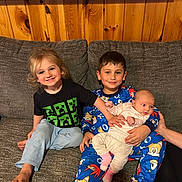 Kash is registered to the contest to win money with this photo: child, baby, pajamas, couch, smile, barefoot, indoor, wood_paneling, family, sibling, holding, happy, clothing, cute, relaxed, portrait, person, infant, casual, seated