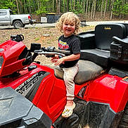 Kash joined the competition — help win amazing prizes! child, blond_hair, curly_hair, atv, red_vehicle, outdoor, woods, truck, tshirt, smiling, crocs, footwear, playful, dirt, grip_handle, seat, nature, daylight, person, vehicle