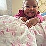 baby, headband, pink_clothing, blanket, unicorn_pattern, rainbow_pattern, indoor, happy, smiling, tongue_out, cute, child, infant, person, hand, face, soft_lighting, cozy, portrait, lying_down