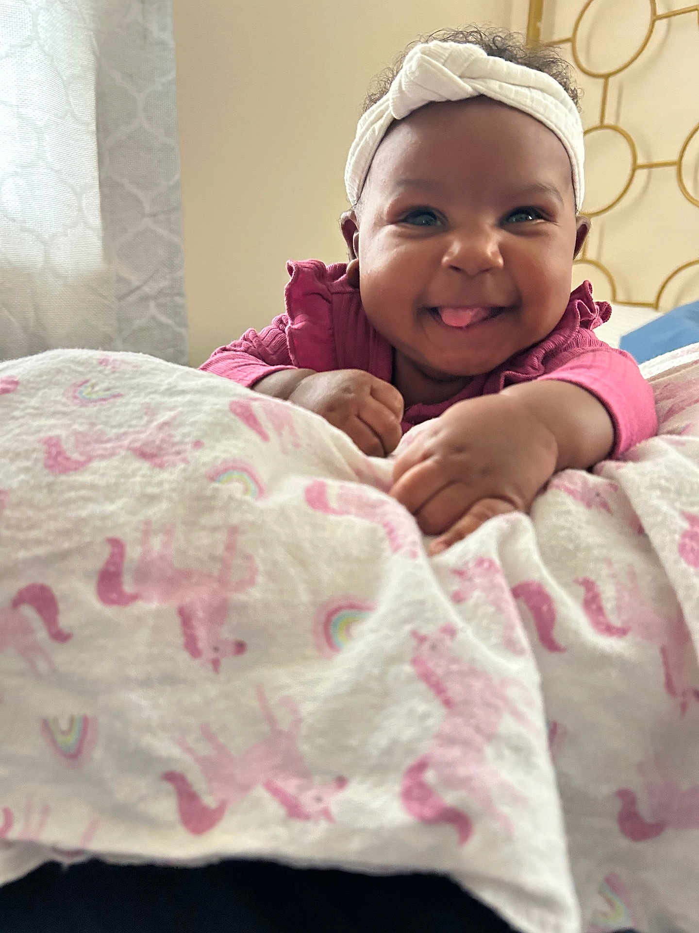 Journey joined the competition — help win amazing prizes! baby, headband, pink_clothing, blanket, unicorn_pattern, rainbow_pattern, indoor, happy, smiling, tongue_out, cute, child, infant, person, hand, face, soft_lighting, cozy, portrait, lying_down