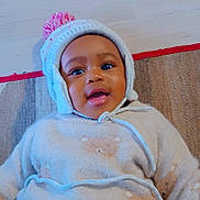 Joyce Ynhelia a rejoint le concours — aidez-le/la à gagner de superbes lots ! baby, child, smiling, hat, pom_pom, sweater, teddy_bear_pattern, indoor, rug, floor, cute, happy, portrait, warm_clothing, infant, face, person, lying_down, cozy, knitwear