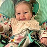 baby, child, smiling, pigtails, bib, onesie, baby_seat, happy, cute, infant, patterned_clothing, indoor, child_seat, colorful, face, person, young_child, cozy, playful, adorable