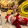 baby, christmas_tree, holiday, presents, ornaments, lights, santa_hat, red_clothing, fluffy_rug, toy, gold_balloon, nutcracker, festive, celebration, indoors, decorations, smiling, cute, winter, holiday_season