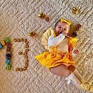 éléna participe au concours pour gagner de l'argent avec cette photo : baby, child, yellow_clothing, bow, lollipop, carpet, easter_eggs, chocolate_bunnies, number_13, smiling, lying_down, sock, cute, festive, indoors, celebration, happy, polka_dot, toddler, playful