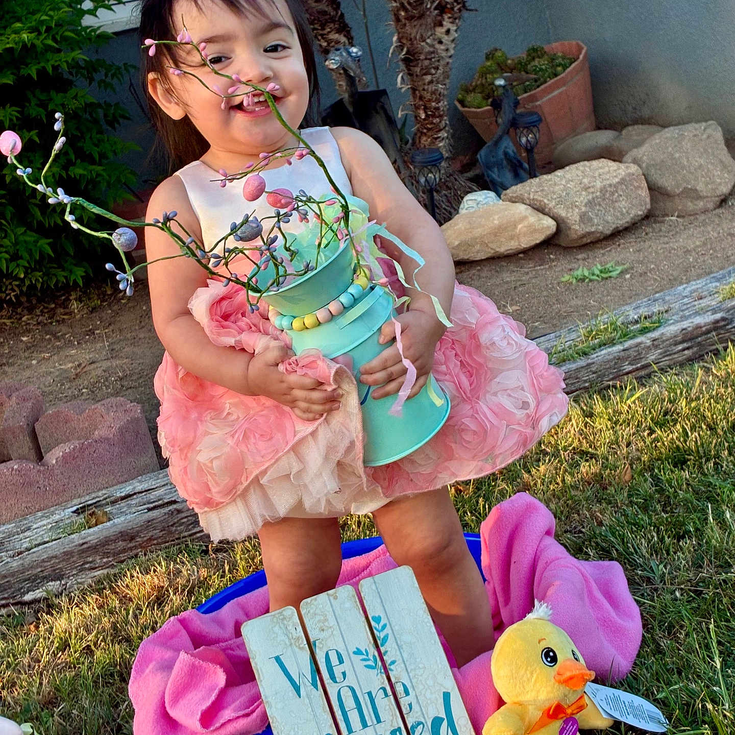 Katalayiah joined the competition — help win amazing prizes! toddler, child, pink_dress, flower_vase, outdoor, grass, toy_duck, sign, happy, smiling, garden, plants, sunlight, decor, playtime, cute, portrait, nature, young_child, holding_object