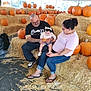 baby, child, adult, pumpkin, hay, tent, family, fall, autumn, orange, clothing, glasses, tattoo, footwear, jeans, sitting, holding, smile, headband, black_tshirt