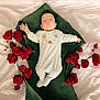 baby, sleeping, onesie, bear_design, red_roses, green_blanket, white_bed_sheet, flower_arrangement, peaceful, infant, cute, soft_lighting, portrait, laying_down, newborn, floral, closeup, adorable, resting, indoors