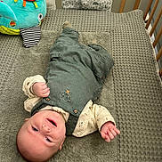 Simon a rejoint le concours — aidez-le/la à gagner de superbes lots ! baby, baby_clothes, blanket, child, crib, cute, fish_toy, green_overalls, happy, indoor, infant, lying_down, patterned_shirt, person, playful, plush_toy, smiling, soft_texture, toddler, wooden_crib