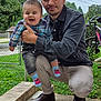 baby, child, man, outdoor, smiling, plaid_shirt, denim_jacket, grass, bike, fence, sidewalk, socks, elmo, casual_clothing, portrait, family, happy, tree, person, daylight