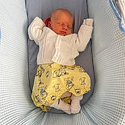 Joshua is registered to the contest to win money with this photo: newborn, baby, sleeping, bassinet, white_sweater, yellow_pants, cartoon_dogs, cozy, soft, textured, infant, cute, child, resting, indoors, head, face, sock, comfort, peaceful