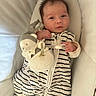 baby, infant, sleeping_sack, plush_toy, soft_toy, striped_clothing, cushion, cozy, child, cute, indoors, resting, comfort, face, person, small_child, baby_garment, smile, toy, lying_down