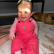 Ivory joined the competition — help win amazing prizes! baby, child, pink_overalls, smiling, indoor, blanket, dog, hair_bows, sitting, cute, happy, person, floor, pattern, clothing, toddler, face, footwear, hand, pet