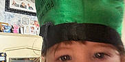 Riley joined the competition — help win amazing prizes! child, face, green_hat, indoor, living_room, furniture, photograph, expression, person, cabinet, decor, portrait, blurry, mouth_open, headwear, curly_hair, wall_art, shelf, household, casual