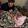 Riley is registered to the contest to win money with this photo: child, toddler, man, bed, blanket, snack, smiling, hair, room, door, furniture, pattern, clothing, interaction, happy, indoor, person, foot, hand, curly_hair