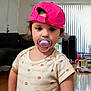 toddler, child, pacifier, pink_cap, indoor, living_room, curtains, couch, wooden_floor, short_sleeve_shirt, person, young_child, face, hair, expressionless, standing, home, window, furniture, daylight