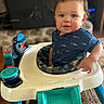 baby, child, toddler, smiling, portrait, indoor, walker, baby_walker, toy, colorful_toy, blue_shirt, shark_pattern, seated, face, brown_hair, home, living_room, carpet, furniture, happy