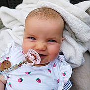 Mya participe au concours pour gagner de l'argent avec cette photo : baby, pacifier, blanket, strawberry_pattern, white_clothing, smiling, face, infant, cute, indoors, soft_texture, child, closeup, happy, person, young_child, clothing, baby_accessory, portrait, comfort