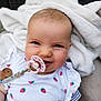 baby, pacifier, blanket, strawberry_pattern, white_clothing, smiling, face, infant, cute, indoors, soft_texture, child, closeup, happy, person, young_child, clothing, baby_accessory, portrait, comfort