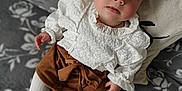Mya participe au concours pour gagner de l'argent avec cette photo : baby, infant, child, white_blouse, brown_skirt, tights, pillow, heart, floral_pattern, blanket, cute, lying_down, indoors, portrait, face, hands, feet, soft_lighting, looking_up, cozy