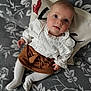 baby, infant, child, white_blouse, brown_skirt, tights, pillow, heart, floral_pattern, blanket, cute, lying_down, indoors, portrait, face, hands, feet, soft_lighting, looking_up, cozy