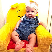 Hazel joined the competition — help win amazing prizes! baby, child, denim_overalls, headband, pink_socks, plush_chair, yellow_chair, smiling, indoor, cute, happy, infant, seated, soft_toys, cozy, portrait, young_child, furniture, childhood, comfortable