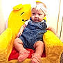 baby, child, denim_overalls, headband, pink_socks, plush_chair, yellow_chair, smiling, indoor, cute, happy, infant, seated, soft_toys, cozy, portrait, young_child, furniture, childhood, comfortable