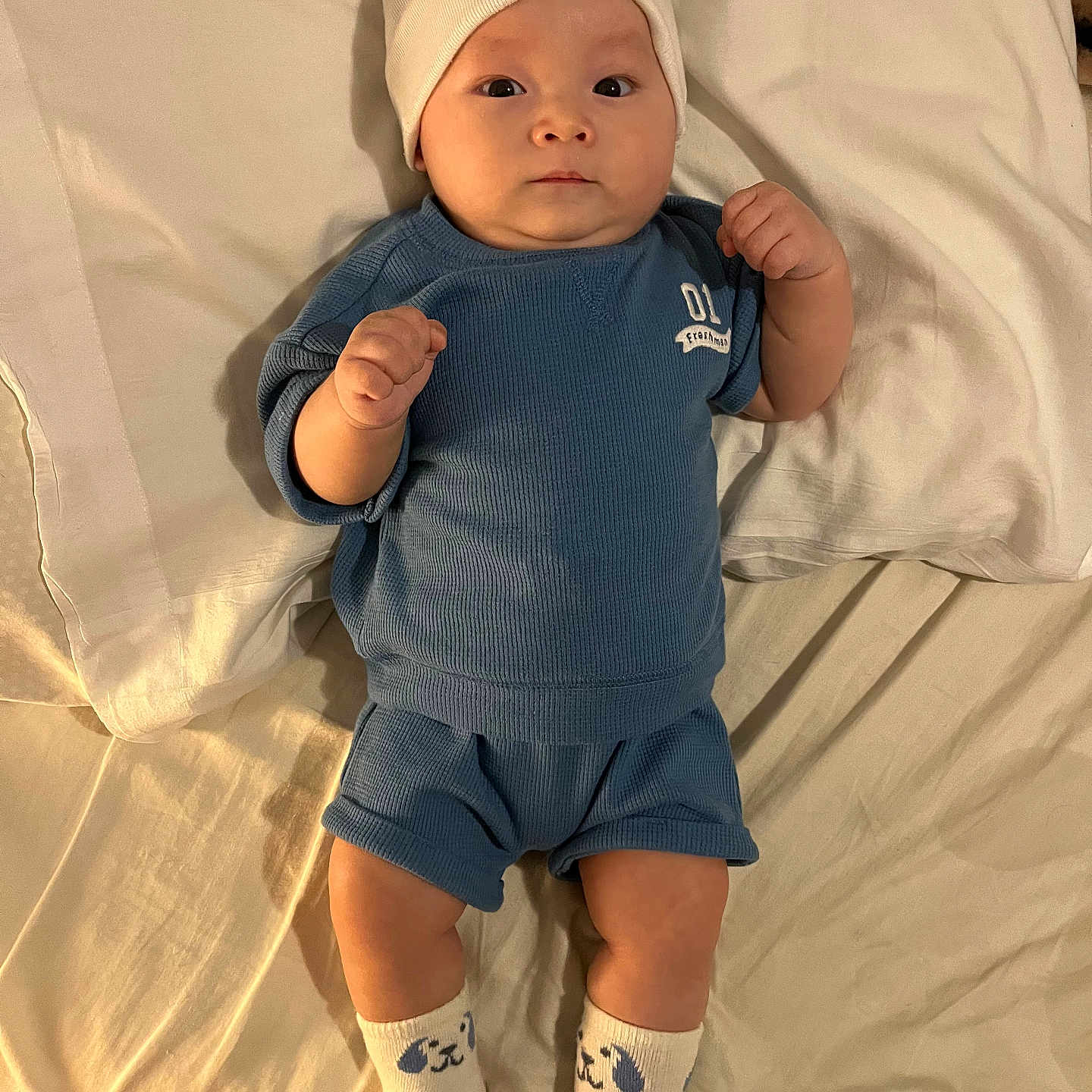 Desmond Dos joined the competition — help win amazing prizes! baby, bed, blue_clothing, child, cozy, cute, expression, hat, indoors, infant, looking_at_camera, lying_down, person, pillow, portrait, sleepwear, small_hands, socks, soft_lighting, white_bedding