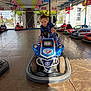 Hadj a rejoint le concours — aidez-le/la à gagner de superbes lots ! amusement_ride, blue, bumper_car, child, daylight, entertainment, floor, fun, happy, helmet, indoor, lights, person, play, police, recreation, ride, smiling, toy_car, vehicle