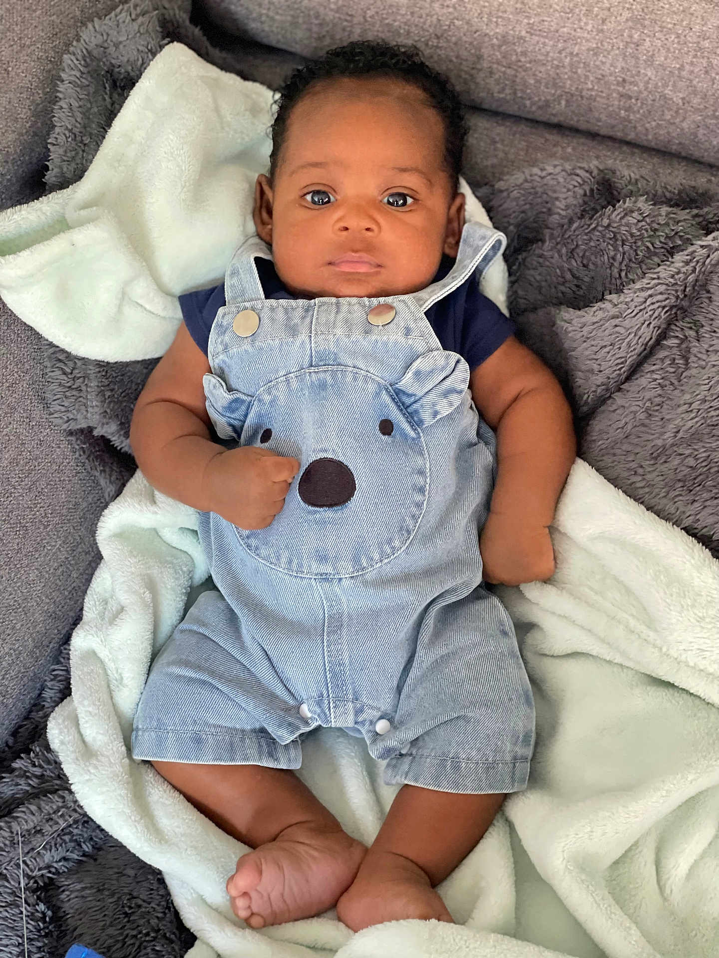 Kenzo a rejoint le concours — aidez-le/la à gagner de superbes lots ! baby, infant, denim_overalls, bear_design, blanket, soft_texture, curious_expression, lying_down, cute, child, foot, hand, skin, clothing, indoors, portrait, comfort, toddler, smiling, young