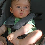 Loann a rejoint le concours — aidez-le/la à gagner de superbes lots ! toddler, child, car_seat, seatbelt, green_shirt, curly_hair, indoors, baby, face, arms, legs, skin, expression, safety, straps, casual_clothing, light, shadow, portrait, candid