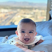 Nathan Benji is registered to the contest to win money with this photo: baby, smiling, infant, face, arm, bed, pillow, indoor, window, cityscape, happy, child, cute, person, skin, clothing, expression, portrait, young, bright