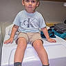 Lynx is registered to the contest to win money with this photo: child, boy, sitting, portrait, indoors, laundry_room, washing_machine, boots, clothing, shorts, shirt, smiling, face, person, wood_paneling, household_appliance, laundry, casual, photography, young