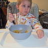 Lynx is registered to the contest to win money with this photo: child, toddler, high_chair, sitting, spoon, bowl, food, meal, dining, indoor, portrait, face, serious, blond_hair, pajamas, baby, tray, kitchen, furniture, home