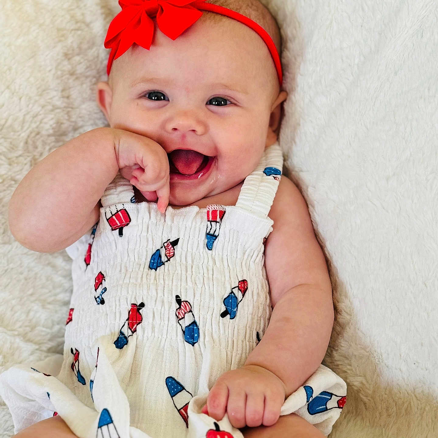 Lakelyn is registered to the contest to win money with this photo: baby, cheerful, child, close_up, cute, expression, hand, happy, headband, indoors, infant, lying_down, one_person, playful, popsicle_print, red_bow, skin, smiling, soft_blanket, white_outfit