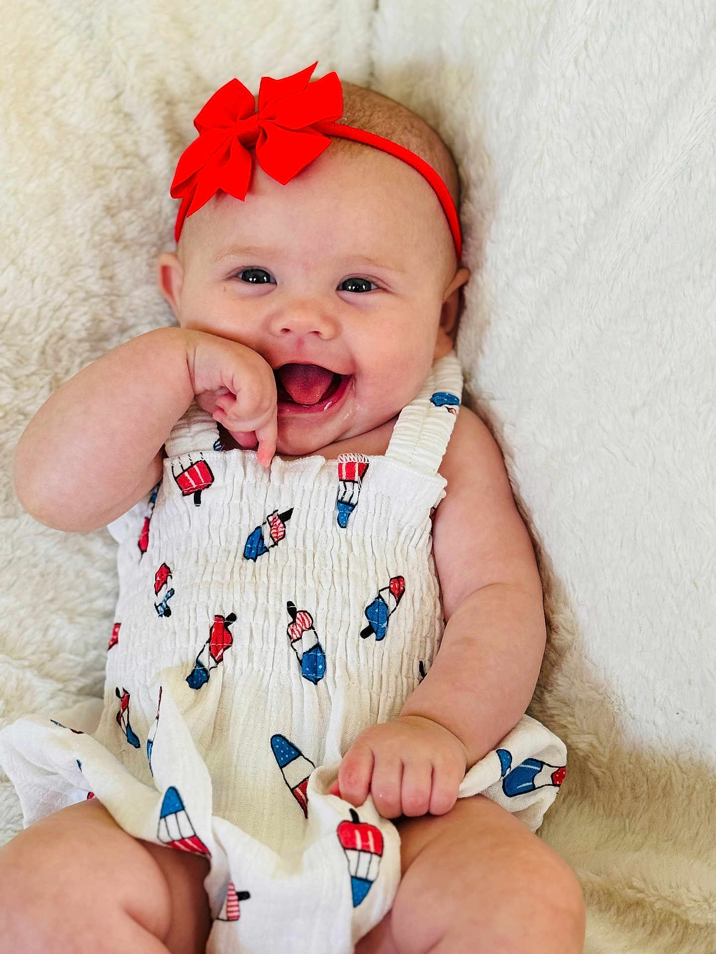 Lakelyn is registered to the contest to win money with this photo: baby, infant, smiling, red_bow, headband, white_outfit, popsicle_print, hand, cheerful, cute, happy, lying_down, soft_blanket, skin, child, one_person, indoors, close_up, expression, playful