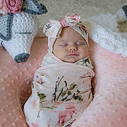 Lakelyn is registered to the contest to win money with this photo: baby, sleeping, swaddle, headband, floral, pink, cushion, crocheted_toy, soft_texture, cozy, infant, peaceful, resting, cute, indoors, portrait, child, wrapped, decor, knitted