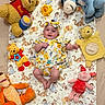baby, child, plush_toy, winnie_the_pooh, piglet, tigger, eeyore, stuffed_animal, blanket, headband, floral_clothing, smiling, lying_down, cute, soft_toys, indoors, colorful, happy, childrens_toy, portrait