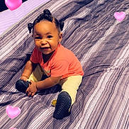 Reign is registered to the contest to win money with this photo: baby, child, smiling, sitting, bed, striped_bedspread, indoor, hair_buns, pink_shirt, yellow_pants, shoes, happy, cute, portrait, heart_emojis, cozy, room, playful, infant, young_child