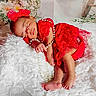 baby, sleeping, red_dress, headband, pearls, blanket, floral_background, infant, cute, peaceful, soft_texture, newborn, portrait, resting, indoors, decor, toddler, hand, foot, skin
